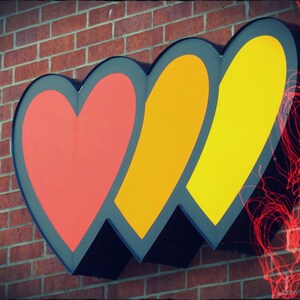 May include: Three interlocking hearts in red, orange, and yellow, painted on a brick wall.