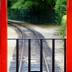 Puede incluir: Un vagón de tren rojo con una ventana que mira hacia un conjunto de vías de tren. Las vías se curvan en la distancia.