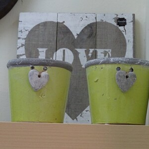 May include: Two green ceramic planters with a heart-shaped design and the word "LOVE" painted on a wooden sign behind them.