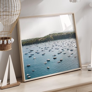 May include: A framed print of a harbor filled with boats, displayed on a light wood dresser. Decorative paper clouds hang from the ceiling. A wicker hot air balloon and wooden sailboats add to the nautical theme.
