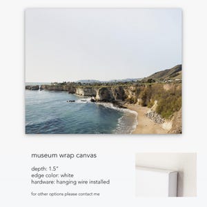 May include: A canvas print of a coastal landscape with a rocky cliffside and a sandy beach. The print has a 1.5 inch depth, white edges, and hanging wire installed.