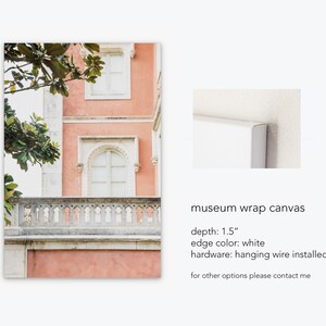 A mockup of a canvas print depicting a pink building with white windows and a stone balcony. The building is surrounded by green trees. the text reads: museum wrap canvas, depth: 1.5”, edge color: white, hardware: hanging wire installed, for other options please contact me.”