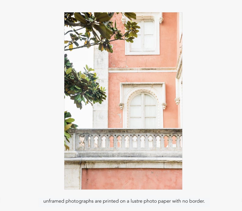 A pink building with white windows and a white balcony. Green leaves from a tree are visible in the upper left corner of the image. Under the photo there is text that reads “unframed photographs are printed on a lustre photo paper with no border.