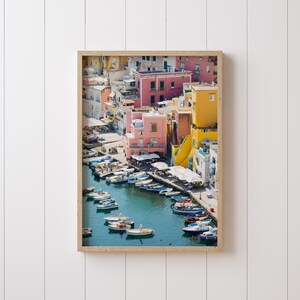May include: An aerial view of a colourful Italian village with a harbour filled with boats. The buildings are painted in shades of pink, yellow, and blue, and the water is a vibrant turquoise.