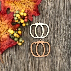 May include: Two unfinished wooden pumpkin cutouts. The pumpkins are outlined and have a stem at the top. The pumpkins are on a wood background.