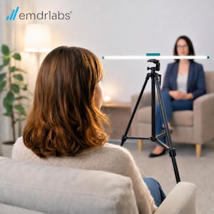 Peut inclure: Un trépied noir supportant une longue barre lumineuse horizontale avec une pièce d'accent bleu sarcelle. Le dispositif est placé entre deux personnes, avec le logo emdrlabs visible dans le coin supérieur gauche de l'image.