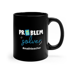 Op de afbeelding: Zwarte koffiemok met een witte afbeelding waarop staat "PROBLEM solver." met een rekenmachine-icoon en de hashtag "#mathteacher".