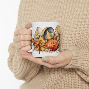 May include: White ceramic mug with a colorful illustration of seashells and a starfish. The seashells are in various shapes and sizes, and some are open to reveal the inside.