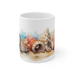 May include: White ceramic mug featuring a watercolour design of seashells on a sandy beach. The seashells are in various colours, including brown, white, orange, and pink.