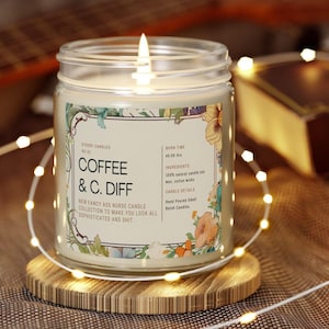 May include: A lit glass jar candle with a floral label that reads "Coffee & C. Diff." The candle sits on a wooden coaster, surrounded by string lights. The label also states "New Fancy Ass Nurse Candle Collection."