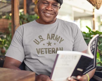 May include: A light gray t-shirt with the text "U.S. ARMY VETERAN" in olive green. The person in the image is wearing a black cap and reading a book. The image is taken outdoors.