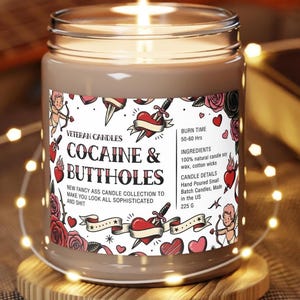 Peut inclure: Une bougie allum&eacute;e dans un bocal en verre avec une &eacute;tiquette indiquant "COCAINE & BUTTHOLES". L'&eacute;tiquette pr&eacute;sente des graphiques de style tatouage de c&oelig;urs, de roses et d'un cupidon. La bougie est sur un dessous de verre en bois et entour&eacute;e de guirlandes lumineuses. La bougie p&egrave;se 225 g.