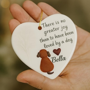 Puede incluir: Adorno de cer&aacute;mica en forma de coraz&oacute;n con una ilustraci&oacute;n de perro y el texto "No hay mayor alegr&iacute;a que haber sido amado por un perro". Presenta un perro marr&oacute;n, un coraz&oacute;n rojo y el nombre "Bella". Incluye una cuerda dorada.