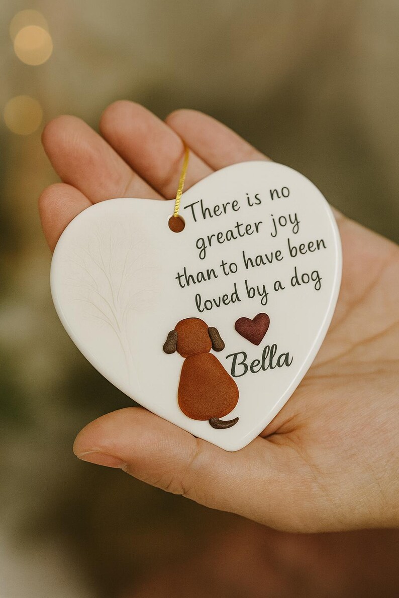 Puede incluir: Adorno de cer&aacute;mica en forma de coraz&oacute;n con una ilustraci&oacute;n de perro y el texto "No hay mayor alegr&iacute;a que haber sido amado por un perro". Presenta un perro marr&oacute;n, un coraz&oacute;n rojo y el nombre "Bella". Incluye una cuerda dorada.