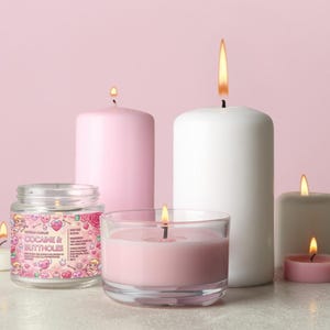 May include: A collection of lit candles in various sizes and shapes, including a jar candle with the text "COCAINE & BUTTHOLES". The candles are in shades of pink, white, and gray, with flames. The background is a solid pink.