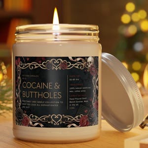 Pu&ograve; includere: Una candela accesa in un barattolo di vetro con un'etichetta nera che recita "COCAINE & BUTTHOLES". L'etichetta include grafiche floreali e di teschio e il testo "NEW FANCY ASS CANDLE COLLECTION TO MAKE YOU LOOK ALL SOPHISTICATED AND SHIT".
