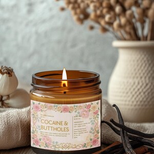 Pu&ograve; includere: Una candela accesa in un barattolo di vetro marrone con un'etichetta floreale che recita "COCAINE & BUTTHOLES". La candela &egrave; appoggiata su una superficie di legno con bastoncini di cannella e baccelli di vaniglia. Un vaso con fiori secchi sullo sfondo.