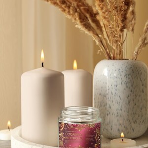 Peut inclure: Composition d&eacute;corative avec trois bougies blanches allum&eacute;es, une petite bougie en pot avec une &eacute;tiquette et un vase avec des plantes s&eacute;ch&eacute;es. L'&eacute;tiquette de la bougie en pot indique "COCAINE & BUTTHOLES". Les objets sont sur un plateau d&eacute;coratif.