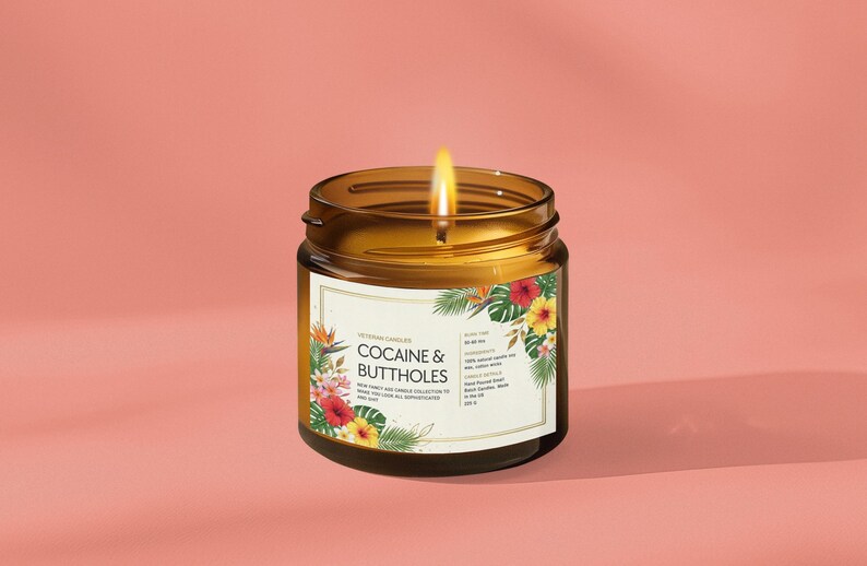 Może przedstawiać: Zapalonego świeca w bursztynowym szklanym słoiku z etykietą z napisem "COCAINE & BUTTHOLES". Etykieta jest ozdobiona tropikalnymi kwiatami i liśćmi. Świeca stoi na r&oacute;żowym tle.