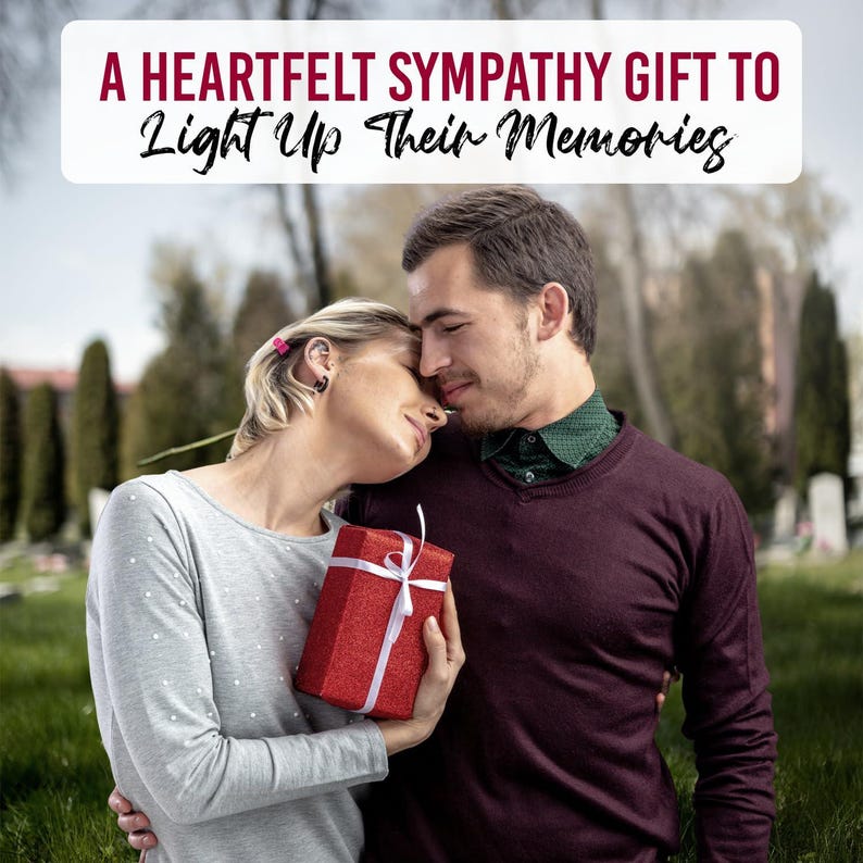 May include: A couple embraces outdoors, with a red gift box tied with a white ribbon. The image includes text that reads, "A Heartfelt Sympathy Gift To Light Up Their Memories."