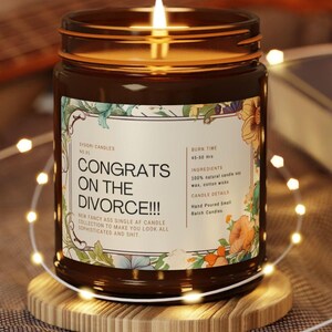 Könnte beinhalten: Eine brennende braune Glas-Kerze mit einem Etikett mit der Aufschrift "CONGRATS ON THE DIVORCE!!!", umgeben von floralen Designs. Die Kerze steht auf einem Holzuntersetzer, mit Lichterketten darum. Die Brenndauer der Kerze beträgt 45-50 Stunden.