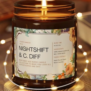 May include: A lit brown glass jar candle with a floral label. The label reads "NIGHTSHIFT & C. DIFF" and "NEW FANCY ASS NURSE CANDLE COLLECTION TO MAKE YOU LOOK ALL SOPHISTICATED AND SHIT." The candle sits on a wooden coaster.