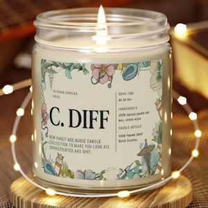 May include: A lit candle in a glass jar with a label that reads "C. DIFF" and "NEW FANCY ASS NURSE CANDLE COLLECTION TO MAKE YOU LOOK ALL SOPHISTICATED AND SHIT." The candle sits on a wooden coaster, surrounded by string lights.