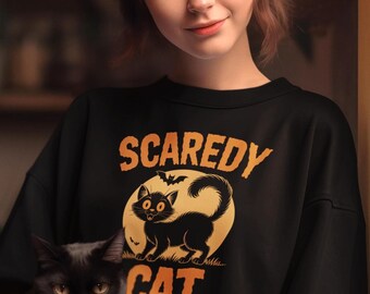 Könnte beinhalten: Schwarzes Sweatshirt mit den Worten "SCAREDY CAT" in orangefarbenen Buchstaben und einer Cartoon-Katze. Eine schwarze Katze wird in den Armen gehalten. Das Sweatshirt ist schwarz.
