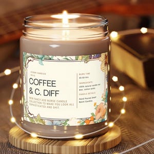 May include: A lit coffee-scented candle in a glass jar with a floral label. The label reads "COFFEE & C. DIFF" and "NEW FANCY ASS NURSE CANDLE COLLECTION TO MAKE YOU LOOK ALL SOPHISTICATED AND SHIT." The candle sits on a wooden coaster.