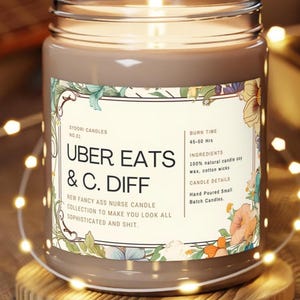 May include: A lit candle in a glass jar with a brown label featuring floral designs and text that reads "UBER EATS & C. DIFF." The label also includes the text "NEW FANCY ASS NURSE CANDLE COLLECTION TO MAKE YOU LOOK ALL SOPHISTICATED AND SHIT."