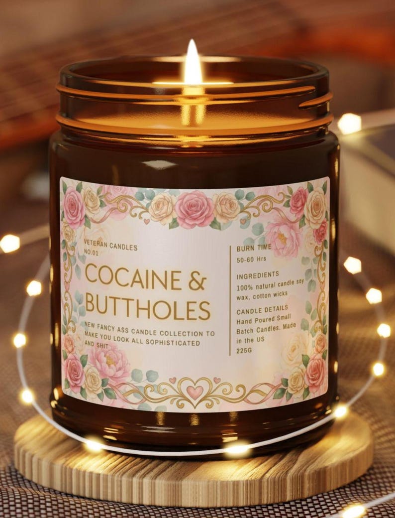Pu&ograve; includere: Una candela accesa in un barattolo di vetro marrone con un'etichetta floreale che recita "COCAINE & BUTTHOLES". L'etichetta include il testo "Veteran Candles" e "New Fancy Ass Candle Collection". La candela &egrave; su un sottobicchiere di legno, circondata da luci a catena.