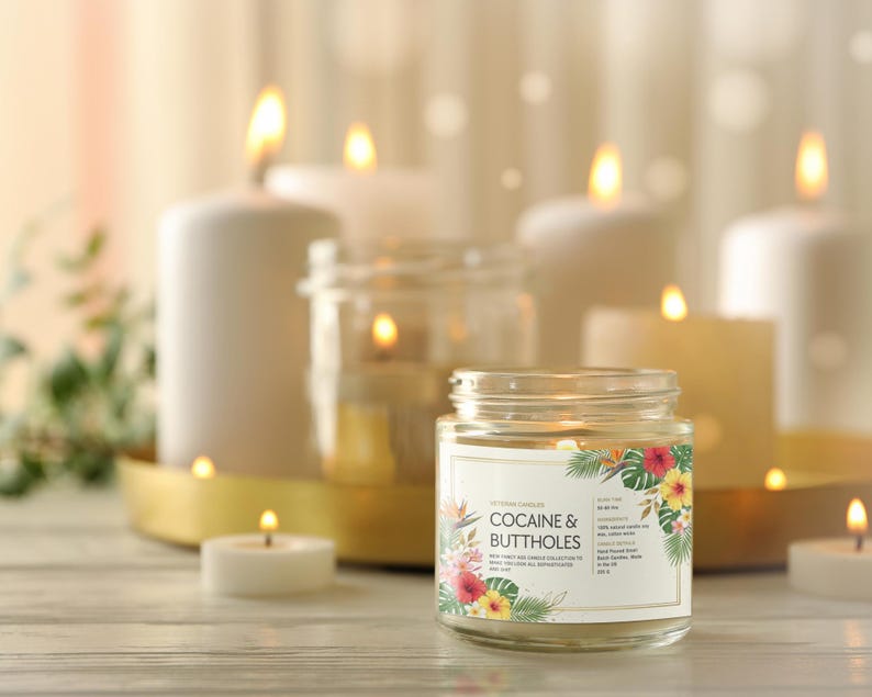 May include: A lit jar candle with a floral label that reads "COCAINE & BUTTHOLES" is the focal point, surrounded by other lit candles of varying sizes. The candles are on a gold tray and a wooden surface.