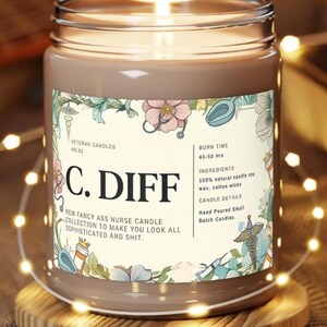 May include: A lit brown candle in a glass jar with a label that reads "C. DIFF." The label includes floral and medical-themed illustrations and text: "NEW FANCY ASS NURSE CANDLE COLLECTION TO MAKE YOU LOOK ALL SOPHISTICATED AND SHIT."