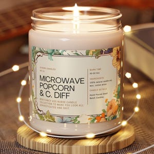 May include: A burning jar candle with a label featuring the text "MICROWAVE POPCORN & C. DIFF" and floral accents. The candle is on a wooden coaster, with fairy lights around it. The label also states the burn time and ingredients.