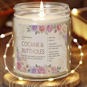May include: A lit glass jar candle with a floral label that reads "COCAINE & BUTTHOLES." The candle is on a wooden coaster and surrounded by string lights. The label also includes the text "NEW FANCY ASS CANDLE COLLECTION TO MAKE YOU LOOK ALL SOPHISTICATED AND SHIT."