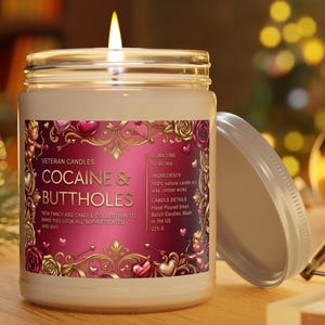 Peut inclure: Une bougie allum&eacute;e dans un bocal en verre avec un couvercle. L'&eacute;tiquette indique "COCAINE & BUTTHOLES" avec du texte suppl&eacute;mentaire. La bougie a une &eacute;tiquette rose et dor&eacute;e avec des &eacute;l&eacute;ments d&eacute;coratifs. Le bocal est sur une surface en bois.