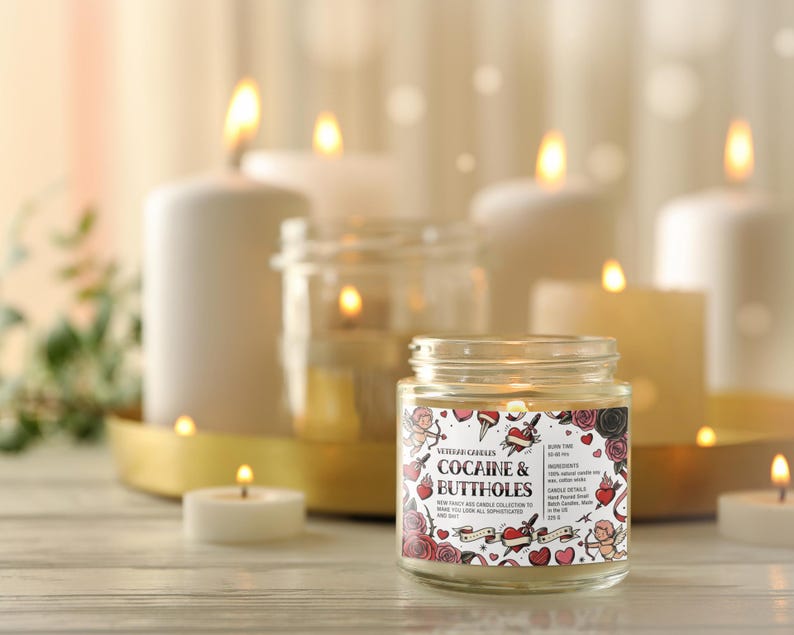 May include: A lit jar candle with the text "Cocaine & Buttholes" on the label, surrounded by roses, hearts, and cherubs. Several other lit candles of varying sizes are in the background, creating a warm, inviting ambiance.