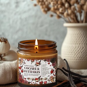 Puede incluir: Una vela encendida en un frasco de vidrio marr&oacute;n con una etiqueta que dice "COCAINE & BUTTHOLES". La vela es parte de la "NEW FANCY ASS CANDLE COLLECTION". La vela est&aacute; rodeada de palitos de canela y vainas de vainilla. La vela tiene un tiempo de combusti&oacute;n de 50-60 horas.