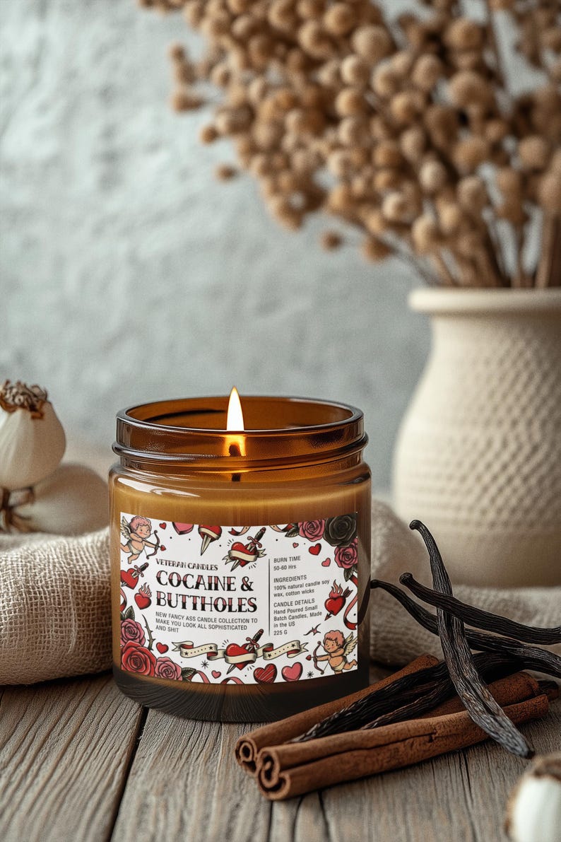 Puede incluir: Una vela encendida en un frasco de vidrio marr&oacute;n con una etiqueta que dice "COCAINE & BUTTHOLES". La vela es parte de la "NEW FANCY ASS CANDLE COLLECTION". La vela est&aacute; rodeada de palitos de canela y vainas de vainilla. La vela tiene un tiempo de combusti&oacute;n de 50-60 horas.