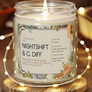 May include: A lit candle in a glass jar with a label that reads "NIGHTSHIFT & C. DIFF." The label includes floral illustrations and text about the candle's ingredients and burn time. The candle sits on a wooden coaster, surrounded by string lights.