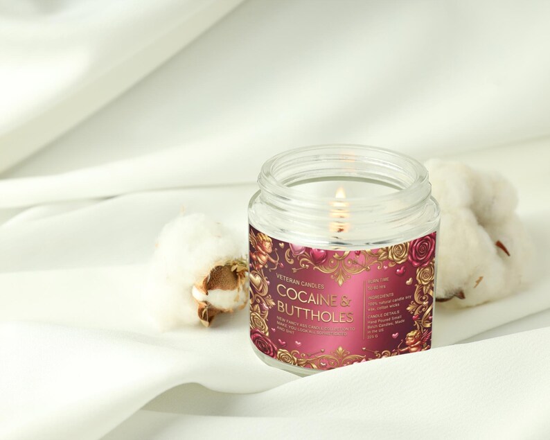 Peut inclure: Une bougie en pot en verre transparent allum&eacute;e avec une &eacute;tiquette qui dit "COCAINE & BUTTHOLES" en lettres dor&eacute;es. L'&eacute;tiquette a un fond bordeaux avec des accents floraux dor&eacute;s. Deux boules de coton sont &agrave; c&ocirc;t&eacute; de la bougie sur une surface blanche.