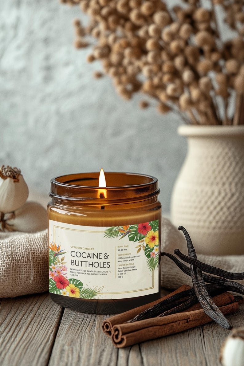 May include: A lit brown glass jar candle with a label featuring floral designs and the text "COCAINE & BUTTHOLES". The candle is surrounded by vanilla beans, cinnamon sticks, and a vase of dried flowers.