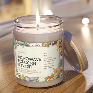 May include: A lit, grey candle in a glass jar with a lid. The label reads "MICROWAVE POPCORN & C. DIFF" with floral accents. The candle has a burn time of 45-50 hours and is made with natural soy wax and cotton wicks.