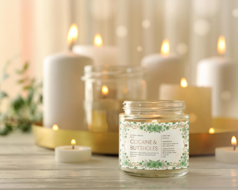 Może przedstawiać: Zapalone świece w szklanym słoiku z etykietą "COCAINE & BUTTHOLES" są w centrum uwagi. Kilka innych zapalonych świec o r&oacute;żnych rozmiarach znajduje się w tle. Świece stoją na drewnianej powierzchni.