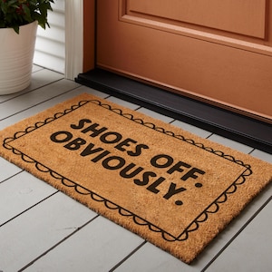 May include: A brown coir doormat with a black border and the text "Shoes Off: Obviously." in black lettering.