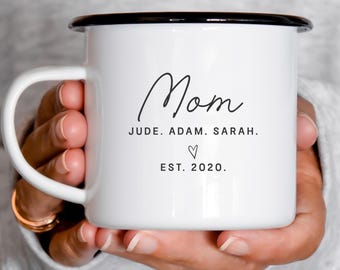 May include: White enamel mug with a black rim and handle. The mug features the word "Mom" in a handwritten font, along with the names Jude, Adam, and Sarah, a heart symbol, and the text "EST. 2020."