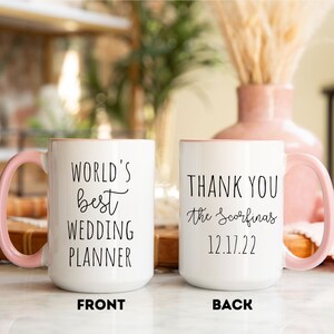 K&ouml;nnte beinhalten: Wei&szlig;er Keramikbecher mit rosa Griff und Rand. Auf der Vorderseite des Bechers steht "WORLD'S best WEDDING PLANNER" in schwarzer Schrift. Auf der R&uuml;ckseite des Bechers steht "THANK YOU the Scorfina's 12.17.22".