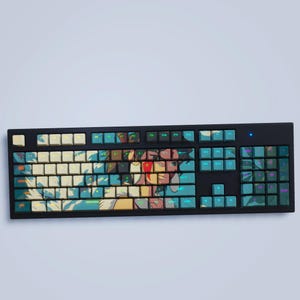 Könnte beinhalten: Eine schwarze mechanische Tastatur mit individuellen Tastenkappen mit einem Anime-Design in Blau-, Gelb- und Rottönen. Die Tastatur hat ein vollständiges Layout mit Nummernblock und Funktionstasten. Die Tastenkappen haben eine matte Oberfläche.