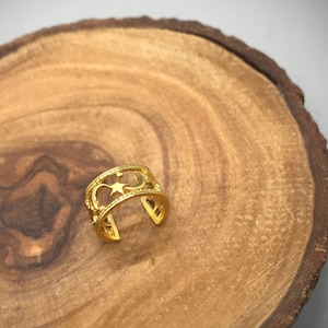 May include: Gold ear cuff with a star and crescent moon design. The cuff is on a wooden surface.