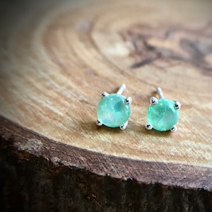 May include: A pair of silver stud earrings with round, light green gemstones.